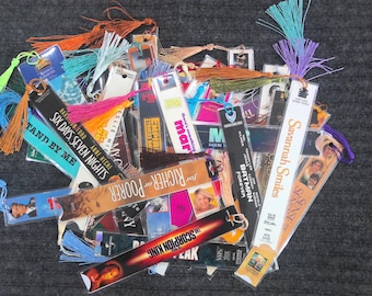 May include: A collection of colorful bookmarks with tassels. The bookmarks feature various movie titles, including "Batman Forever", "Six Days Seven Nights", "Richer Poorer", and "The Scorpion King".