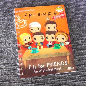 May include: Spiral-bound "F is for Friends" alphabet book. The cover features cartoon figures from the TV show "Friends" and the text "Little Golden Book" and "Funko". The background is orange with a coffee cup graphic.