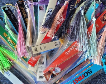 May include: A collection of colorful tassel bookmarks with various designs and patterns. The bookmarks are made of different materials, including fabric, ribbon, and paper. Some of the bookmarks have text on them, such as "The Right Book" and "Star Wars".