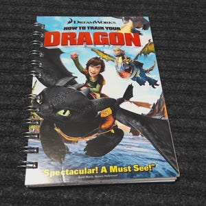 May include: A spiral-bound notebook featuring the DreamWorks movie "How to Train Your Dragon." The cover art depicts a black dragon with a rider, and other dragons in flight. The title is in red and the tagline reads "Spectacular! A Must See!"