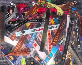 May include: A collection of colorful bookmarks with tassels. The bookmarks feature various designs, including movie titles like "Godzilla," "Superman," and "Raiders of the Lost Ark." Some have text like "Happyess" and "Chipmunks."