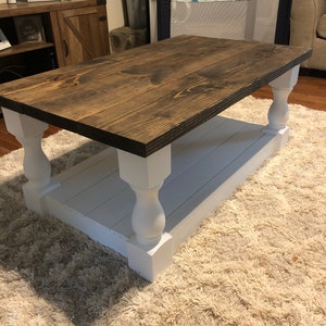 May include: A dark brown wooden coffee table with white painted legs and a white shelf. The table is sitting on a light brown shag rug.