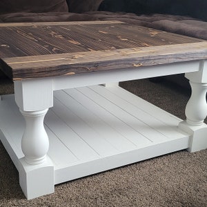 May include: A square coffee table with a dark wood top and white painted base. The base has turned legs and a lower shelf.