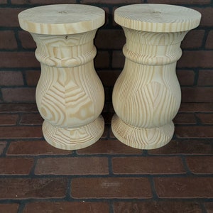 May include: Two unfinished wooden table legs with a turned design. The legs are made of light-colored wood and have a smooth, polished finish.