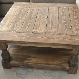 May include: A rustic wooden coffee table with a dark brown stain. The table has a lower shelf and turned legs.