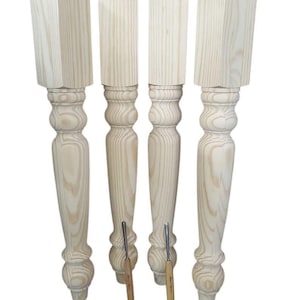 May include: Four unfinished wooden table legs with a turned design. The legs are hand-turned and have a square top.