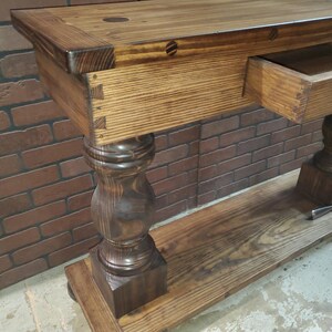 May include: A dark brown wooden console table with a single drawer and turned legs. The table has a distressed finish and is made of solid wood.