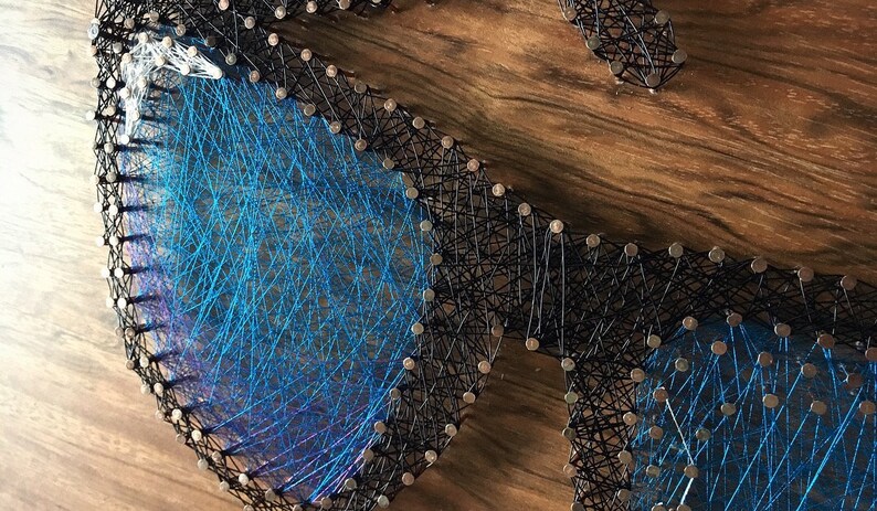 May include: A handmade string art piece depicting a pair of sunglasses. The sunglasses are crafted with black string outlining the frames and blue string filling the lenses. The piece is mounted on a wooden surface.