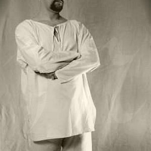 May include: A man wearing a white, long-sleeved shirt with a crew neck and a short-sleeved white undershirt. He is standing with his arms crossed in front of him.