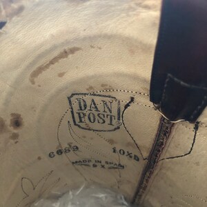 Puede incluir: Vista interior de una bota de vaquero de cuero marr&oacute;n. La plantilla presenta el logotipo "DAN POST", indicaciones de talla y el texto "MADE IN SPAIN". El interior de la bota muestra desgaste.