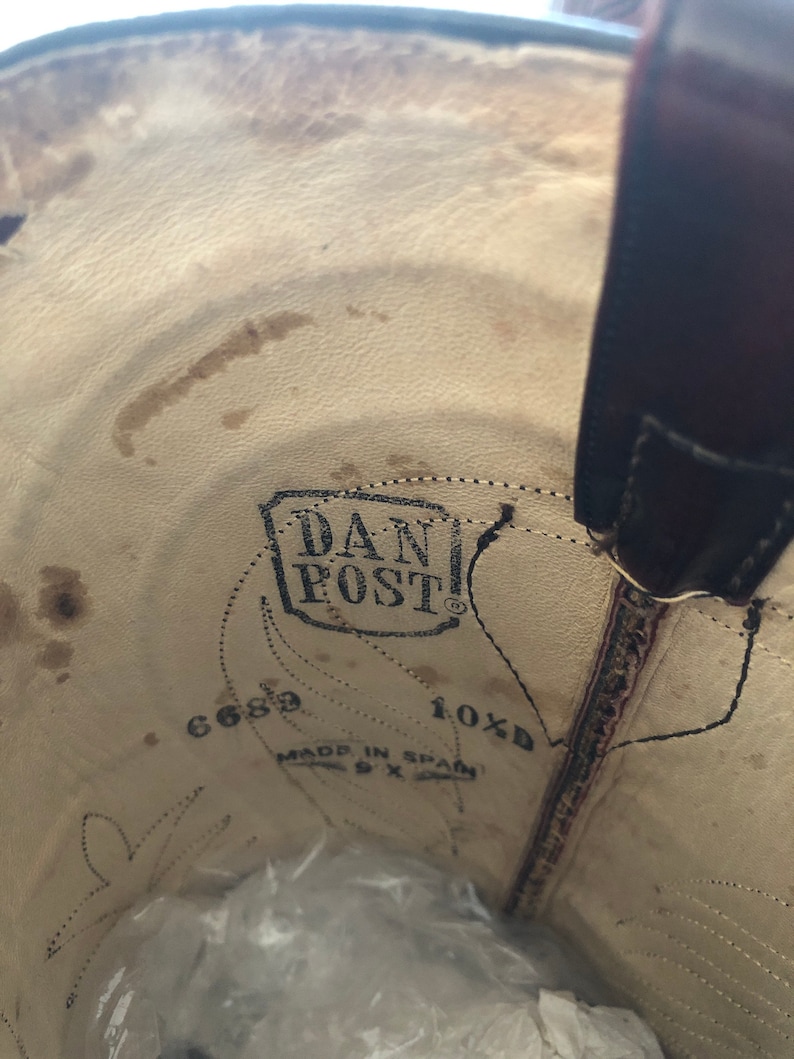 Puede incluir: Vista interior de una bota de vaquero de cuero marr&oacute;n. La plantilla presenta el logotipo "DAN POST", indicaciones de talla y el texto "MADE IN SPAIN". El interior de la bota muestra desgaste.