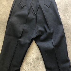 May include: Black dress pants with a unique back design. The pants have a high waist with decorative pointed accents on the back waistband. The fabric appears to be a smooth, solid color, and the pants have a classic, tailored fit.