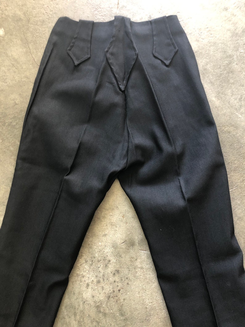 May include: Black dress pants with a unique back design. The pants have a high waist with decorative pointed accents on the back waistband. The fabric appears to be a smooth, solid color, and the pants have a classic, tailored fit.