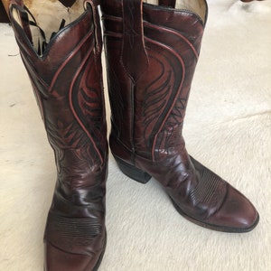Puede incluir: Un par de botas de vaquero burdeos con intrincados dise&ntilde;os de costura. Las botas tienen puntas puntiagudas, presillas y un estilo occidental cl&aacute;sico. El cuero parece desgastado, lo que aumenta su atractivo vintage.