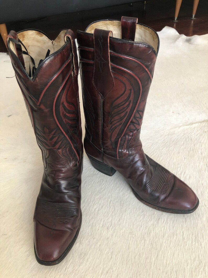 Puede incluir: Un par de botas de vaquero burdeos con intrincados dise&ntilde;os de costura. Las botas tienen puntas puntiagudas, presillas y un estilo occidental cl&aacute;sico. El cuero parece desgastado, lo que aumenta su atractivo vintage.
