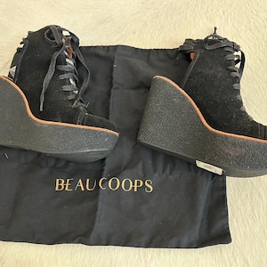 May include: Black suede wedge sneakers with lace-up closure. The shoes have a thick, textured sole and a wedge heel. The brand name "BEAU COOPS" is printed on a black fabric bag.