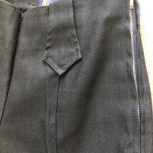 May include: Close-up of black pants with a side zipper. The pants have a diamond-shaped detail at the waist and a tag that reads "Parkhandle Slim". The fabric appears to be a sturdy, dark material.