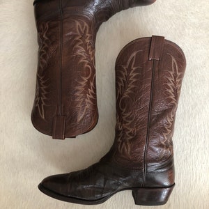 Könnte beinhalten: Ein Paar braune Leder-Cowboystiefel. Die Stiefel haben dekorative Nähte und eine spitze Zehenpartie. Das Leder hat einen Used-Look. Die Stiefel sind ein klassischer Western-Stil.