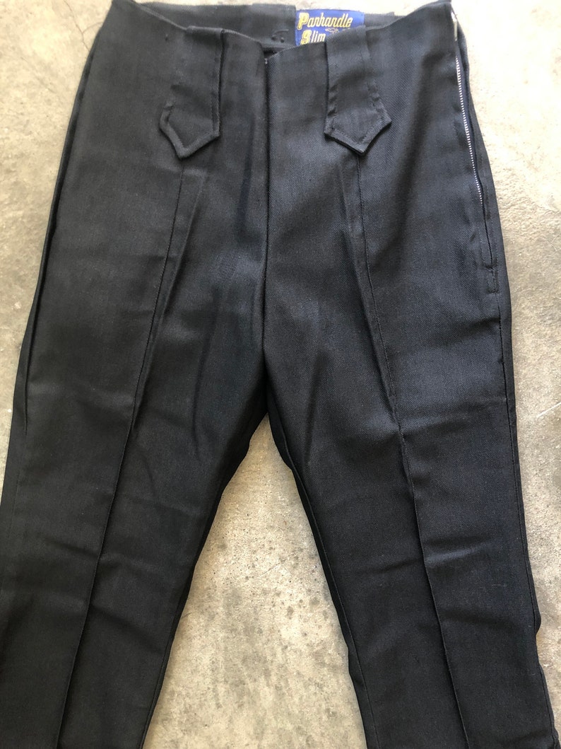 May include: Black pants with a side zipper and decorative waist details. The pants have a label that reads "Panhandle Slim". The pants are made of a dark fabric.