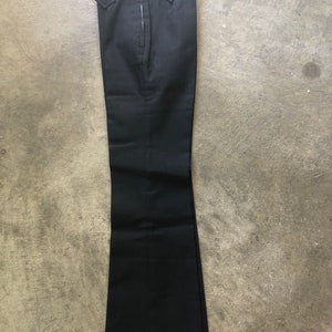 May include: Black flared pants with a zipper closure. The pants have a high waist and two small pockets. The fabric appears to be a solid, dark color. The pants are laid flat on a concrete surface.