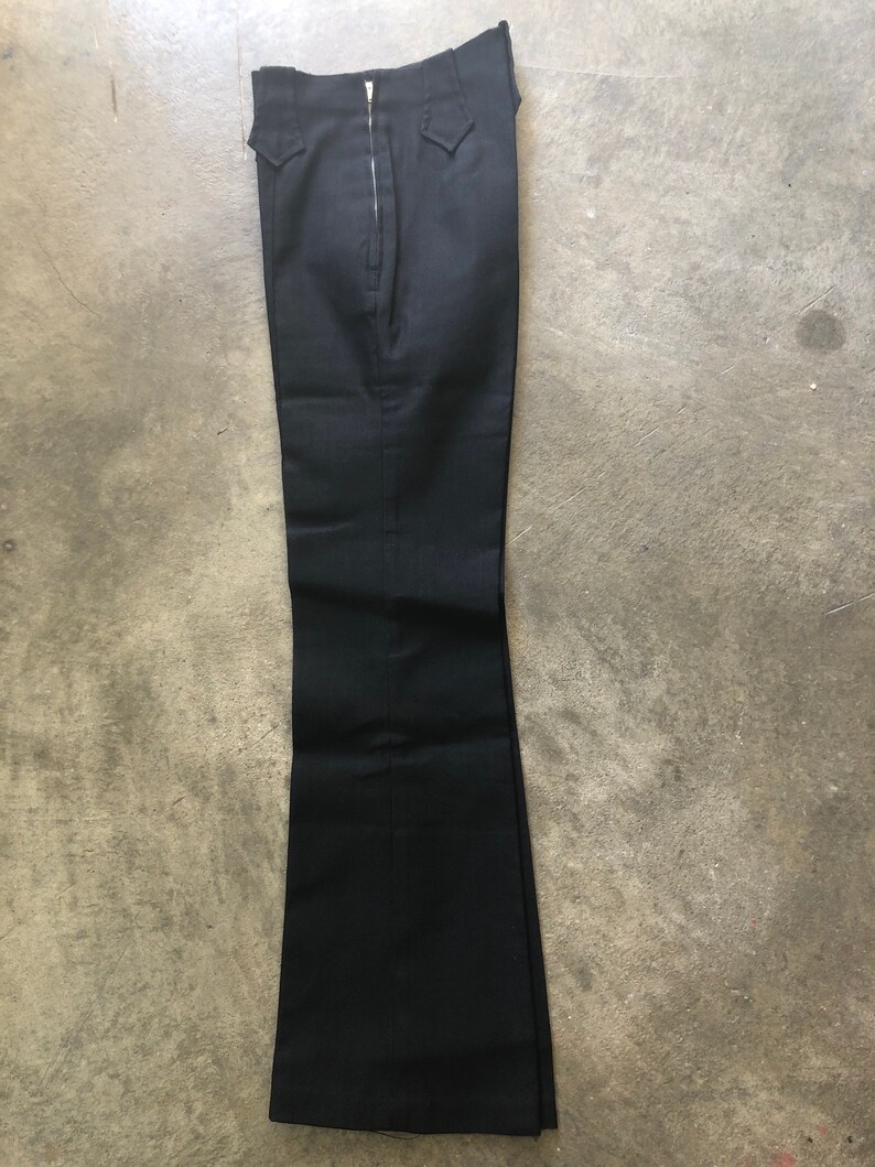 May include: Black flared pants with a zipper closure. The pants have a high waist and two small pockets. The fabric appears to be a solid, dark color. The pants are laid flat on a concrete surface.