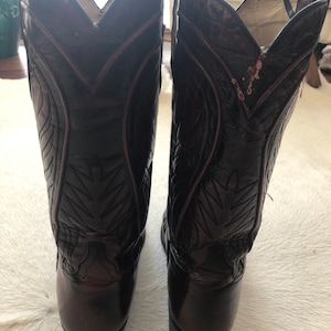 Puede incluir: Un par de botas de vaquero marrones oscuras con costuras decorativas y punta afilada. Las botas tienen un acabado brillante y est&aacute;n hechas de cuero. Las botas son de estilo Western cl&aacute;sico.