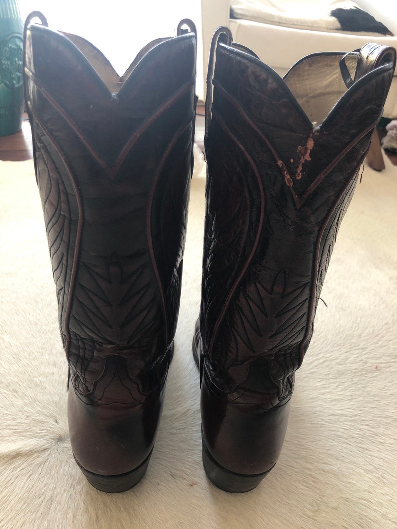 Puede incluir: Un par de botas de vaquero marrones oscuras con costuras decorativas y punta afilada. Las botas tienen un acabado brillante y est&aacute;n hechas de cuero. Las botas son de estilo Western cl&aacute;sico.