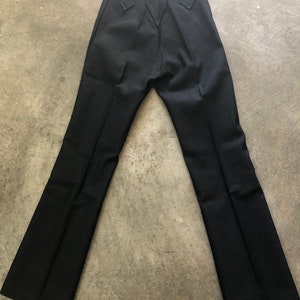 May include: Black pants with a flared leg design. The pants have a high waist and decorative stitching on the back pockets. The pants are made of a smooth, dark fabric.