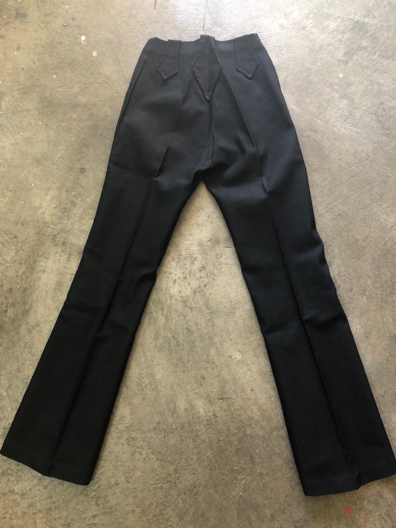 May include: Black pants with a flared leg design. The pants have a high waist and decorative stitching on the back pockets. The pants are made of a smooth, dark fabric.