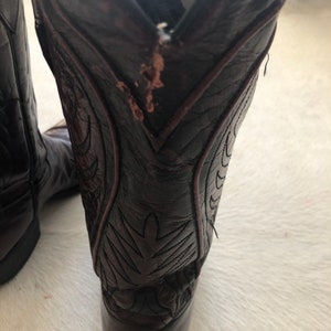 Puede incluir: Botas de vaquero de cuero marr&oacute;n oscuro con costuras decorativas. Las botas tienen una puntera puntiaguda y un tac&oacute;n apilado. El cuero muestra algo de desgaste. Las botas est&aacute;n dise&ntilde;adas para montar a caballo y trabajar.