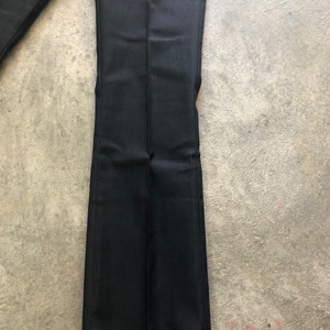 May include: Black dress pants with a slight flare at the bottom. The pants are made of a smooth, dark fabric and have a center crease down the front of each leg. The pants are laying on a gray surface.