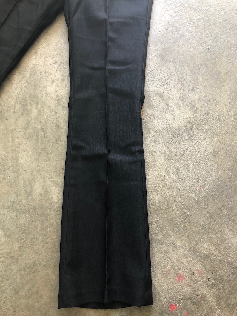 May include: Black dress pants with a slight flare at the bottom. The pants are made of a smooth, dark fabric and have a center crease down the front of each leg. The pants are laying on a gray surface.
