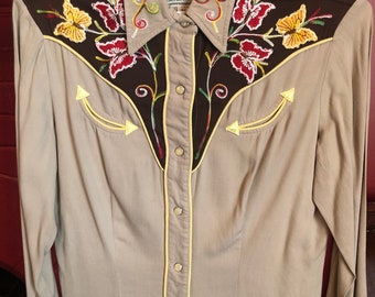 May include: Tan button-down shirt with brown shoulder yokes and collar. The shirt features colorful floral embroidery on the yoke and front panels, with yellow arrow details. The collar has the text "CALIFORNIA RANCHWEAR".