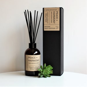 May include: A brown glass bottle with black reeds and a black box. The bottle has a label that reads "Peace + Harmony" and "Earthy Meditative Aroma". The box has a label that reads "Peace + Harmony" and "Artisan Reed Diffuser 07".