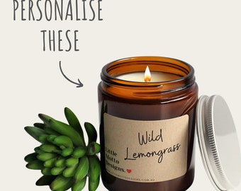 Op de afbeelding: Een bruine glazen kaars pot met een wit deksel. De kaars is aangestoken en de pot heeft een bruin papieren etiket met de tekst "Wild Lemongrass" en "Little Motto Designs".