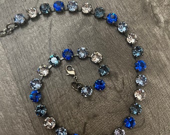 May include: A delicate necklace with a gradient of blue, gray, and clear crystals. The necklace is made of small, round crystals that are connected by silver-toned metal.