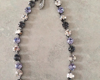 May include: A silver necklace with a gradient of clear, light purple, and dark purple crystals. The necklace has a silver leaf charm.