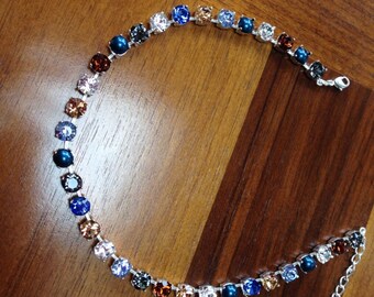 May include: A silver chain necklace with a row of colorful round rhinestones. The rhinestones are arranged in a gradient pattern, starting with brown and transitioning to blue.
