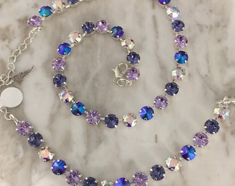 May include: A delicate necklace featuring a series of iridescent, round crystals in shades of purple, blue, and clear. The crystals are set in a silver-toned metal chain, with a lobster clasp closure and an adjustable length.