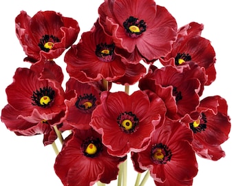 Puede incluir: Un ramo de amapolas artificiales de color rojo intenso con pétalos ondulados, cada una con un prominente anillo de estambres negros que rodea un centro amarillo brillante, unidas a tallos delgados de color verde claro sobre fondo blanco.