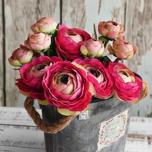 May include: A display of pink and red artificial flowers in a galvanised metal bucket with a rope handle. The bucket has a decorative label that reads "Welcome to my garden."
