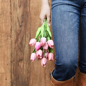 K&ouml;nnte beinhalten: Ein Strau&szlig; rosa Tulpen, gehalten von einer Person in blauen Jeans und braunen Stiefeln.