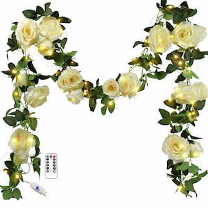 May include: A decorative garland featuring cream-coloured roses and green leaves, strung with small, warm white LED lights. Includes a remote control and a USB connector. Suitable for home or event decoration.