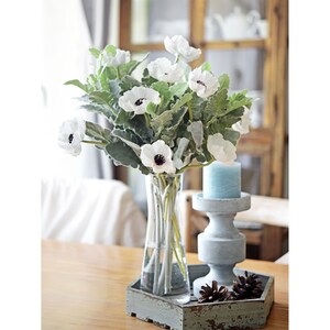 May include: A bouquet of white anemones with dark centers in a clear glass vase on a rustic wooden tray with a blue candle holder.