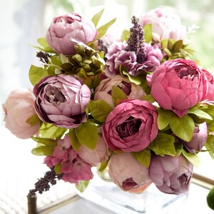 Puede incluir: Un ramo de peon&iacute;as artificiales de color rosa y flores moradas con hojas verdes.