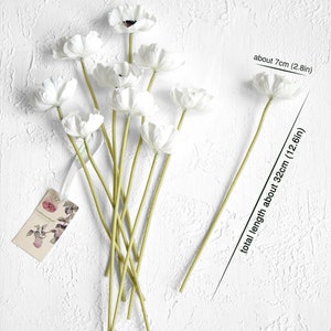 May include: A bouquet of 9 white artificial anemones with green stems. The flowers are about 7 cm (2.8 in) wide and the stems are about 32 cm (12.6 in) long.