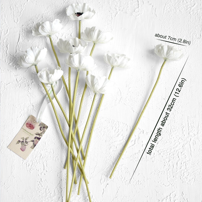 May include: A bouquet of 9 white artificial anemones with green stems. The flowers are about 7 cm (2.8 in) wide and the stems are about 32 cm (12.6 in) long.