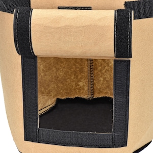 May include: A brown fabric grow bag with black velcro straps and a black fabric window. The bag is designed for planting and growing plants.
