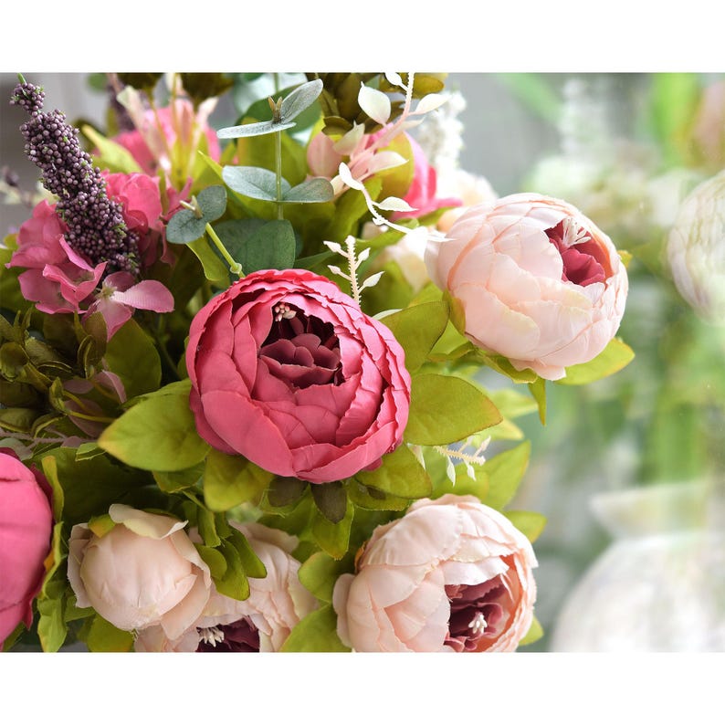 Puede incluir: Un ramo de flores artificiales con peon&iacute;as rosas y rojas, hojas verdes y ramitas moradas.
