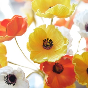 Puede incluir: Un ramo de flores de seda con p&eacute;talos de color naranja, amarillo y blanco. Las flores est&aacute;n dispuestas en un jarr&oacute;n y tienen un aspecto realista.